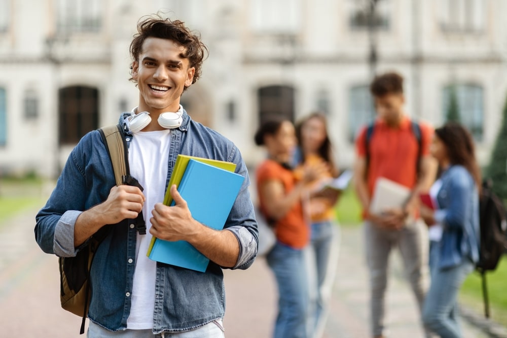 Smiling college student holding books and backpack on campus