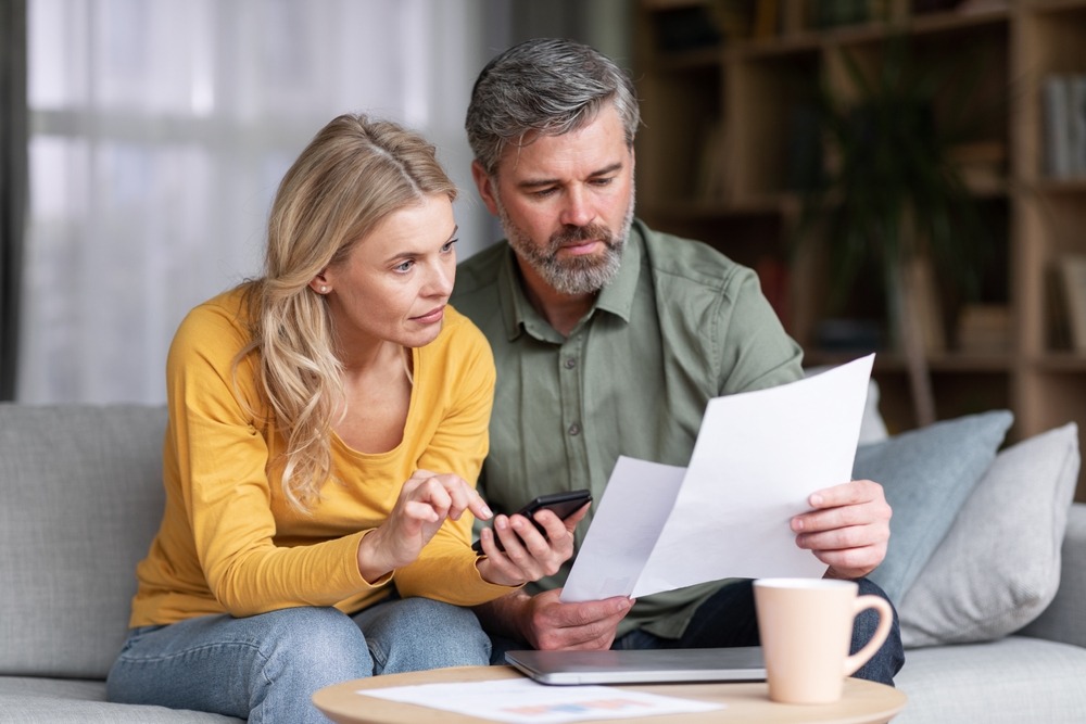Concerned couple reviewing bankruptcy paperwork and using a smartphone to research Chapter 7 filing costs.