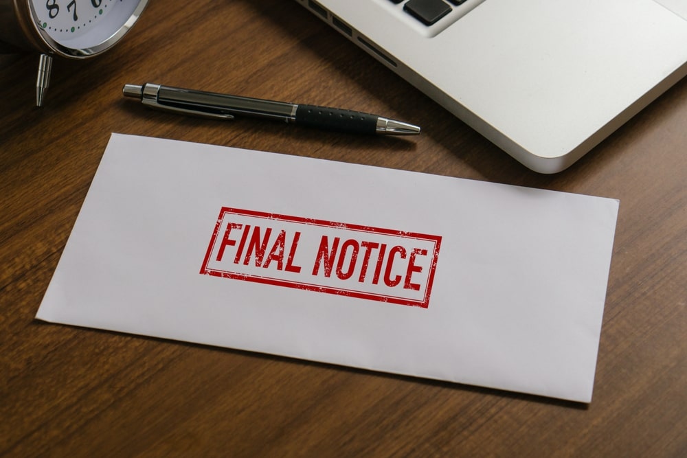 Final notice envelope on desk next to laptop and pen
