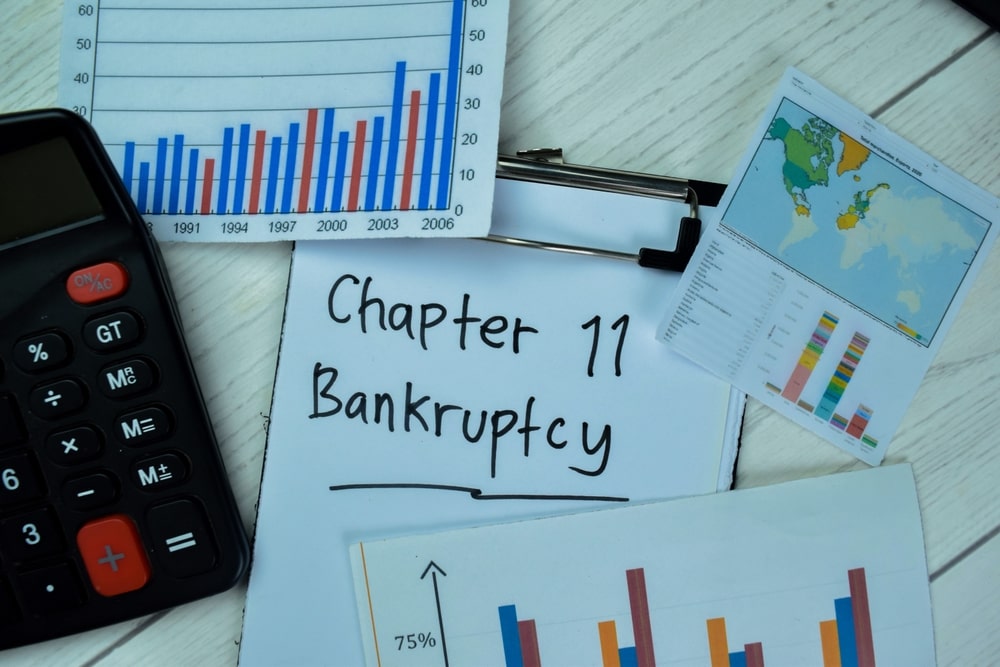 Charts, graphs, and calculator surrounding clipboard with Chapter 11 Bankruptcy text