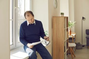 Man sitting by the window reviewing paperwork with a thoughtful expression