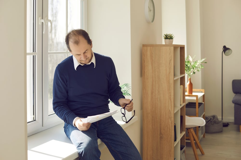 Man sitting by the window reviewing paperwork with a thoughtful expression