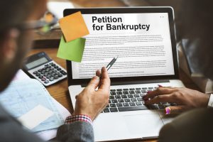 Two people reviewing a bankruptcy petition on a laptop with documents and a calculator nearby