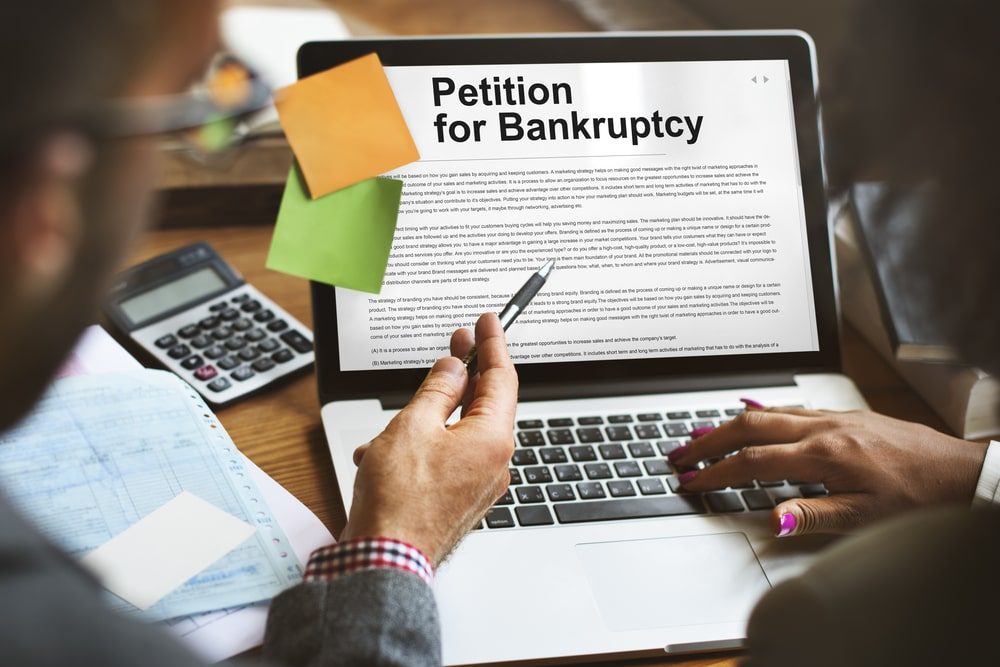 Two people reviewing a bankruptcy petition on a laptop with documents and a calculator nearby