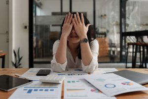 Stressed woman covering her face while sitting at a desk full of financial documents