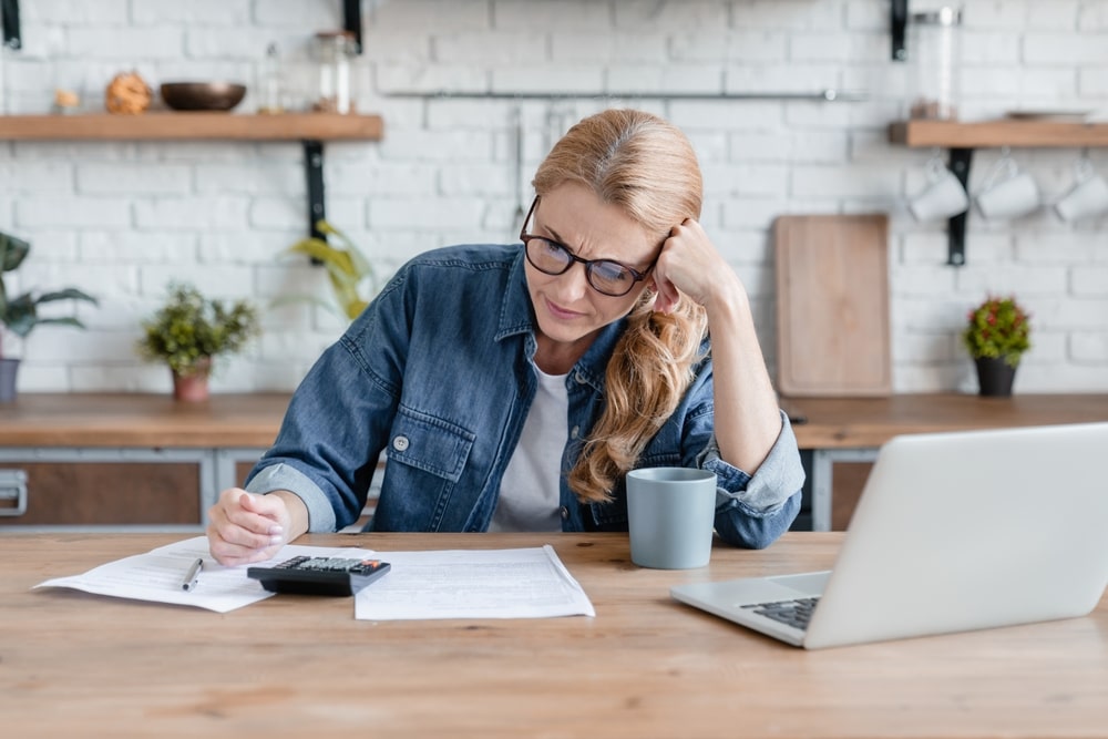 Woman reviewing bankruptcy paperwork at the kitchen table with a calculator and a laptop