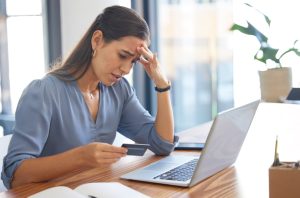 Stressed woman holding credit card while looking at laptop screen
