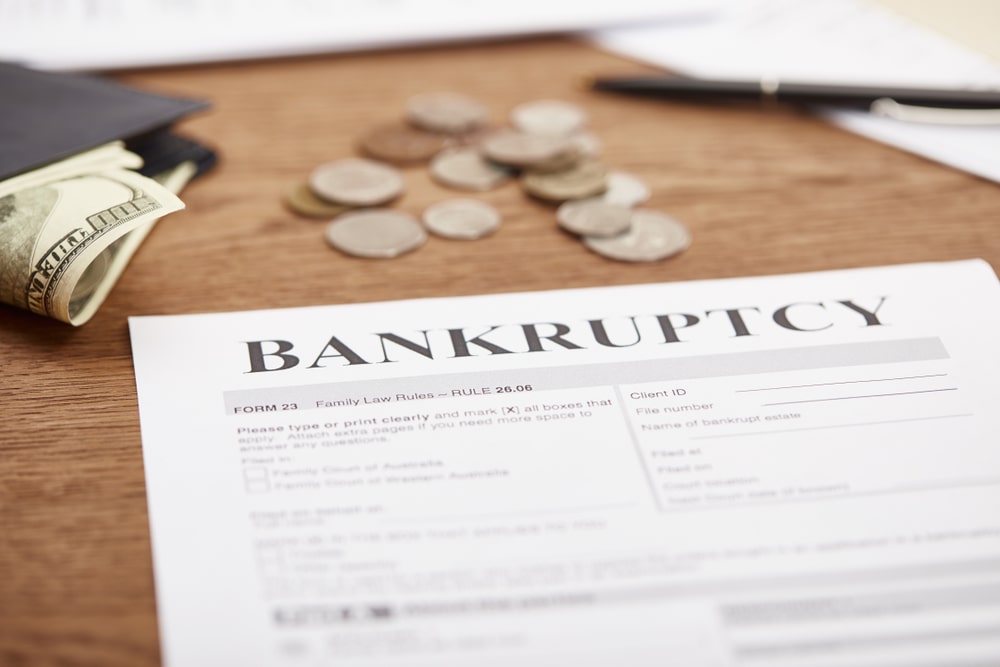 Bankruptcy document with scattered coins, cash, and a wallet on a wooden table