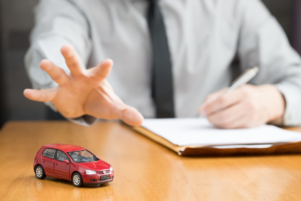 Businessman reaching for a red toy car on a desk, symbolizing legal efforts to protect a vehicle during bankruptcy filing.