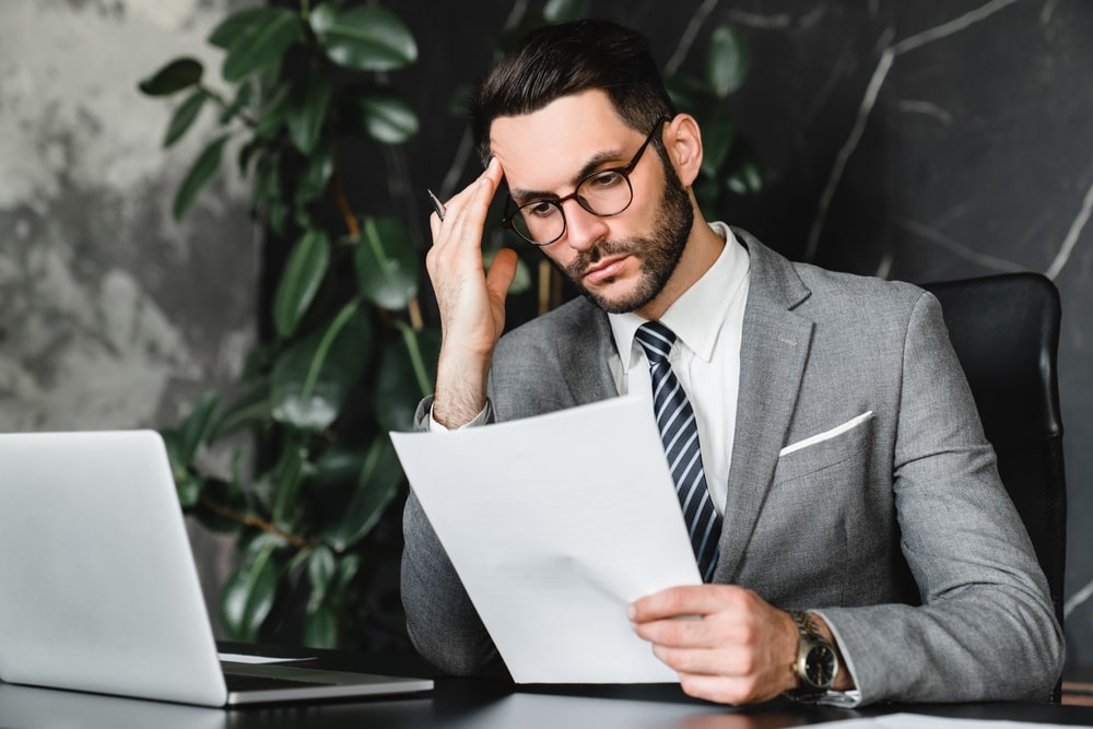 Stressed businessman in a suit reading bankruptcy paperwork at a desk