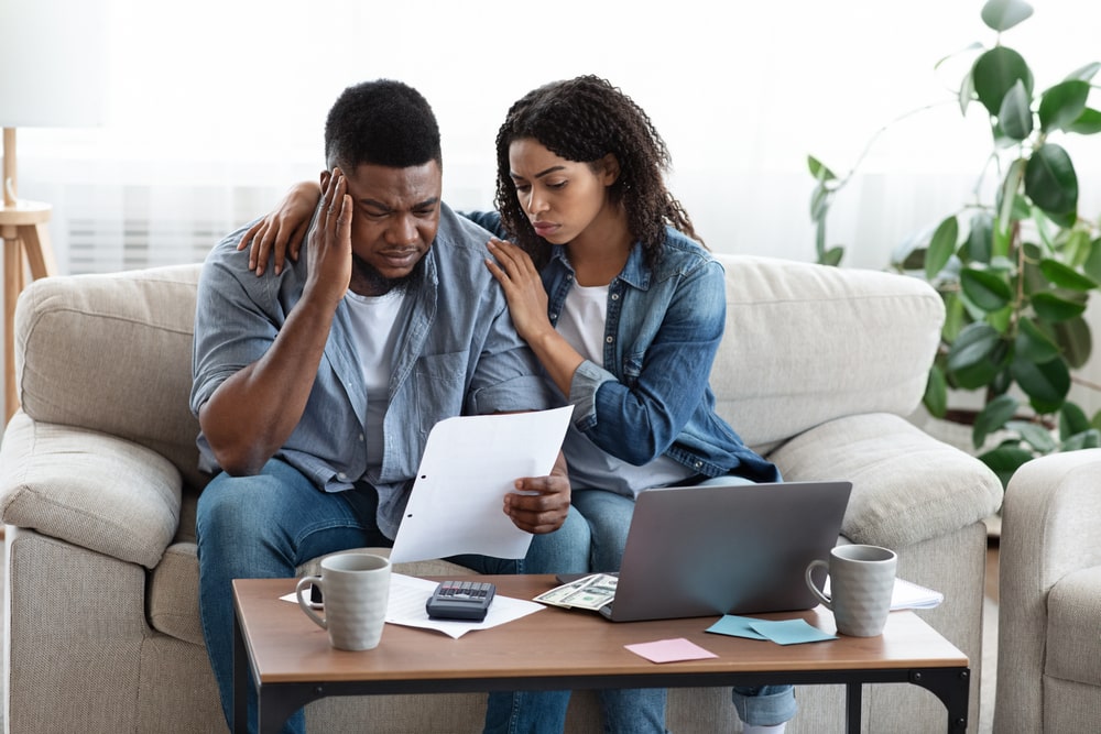 Stressed couple reviewing financial documents with a laptop and calculator while considering how to file bankruptcy for debt.