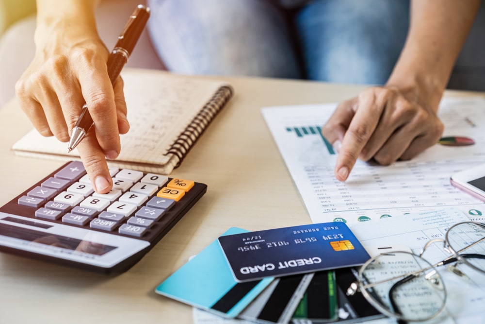 Hands using calculator and pointing at a financial chart beside credit cards