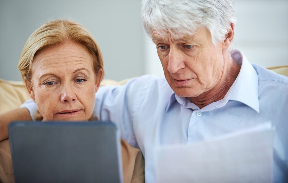A senior couple reviewing bankruptcy filing steps on a tablet and paperwork
