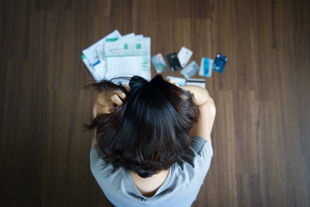Overhead view of a stressed woman surrounded by credit cards and bills on the floor