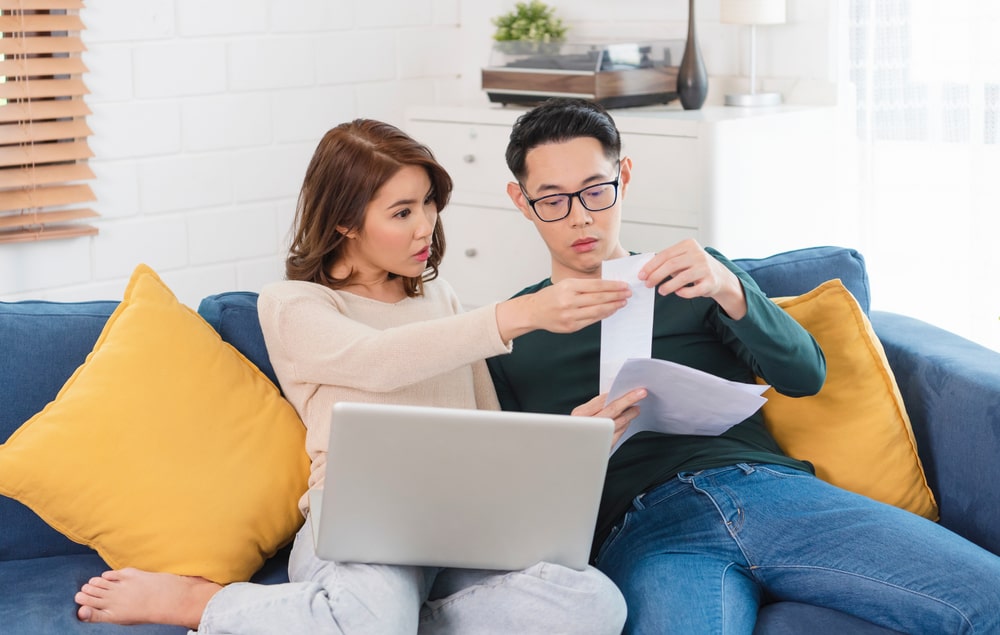 A concerned couple reviewing financial documents together on the sofa with a laptop
