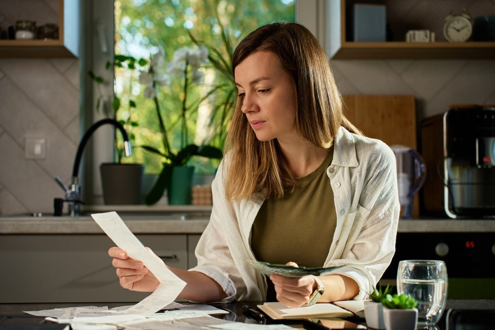 Woman sitting at kitchen table calculating bills and expenses