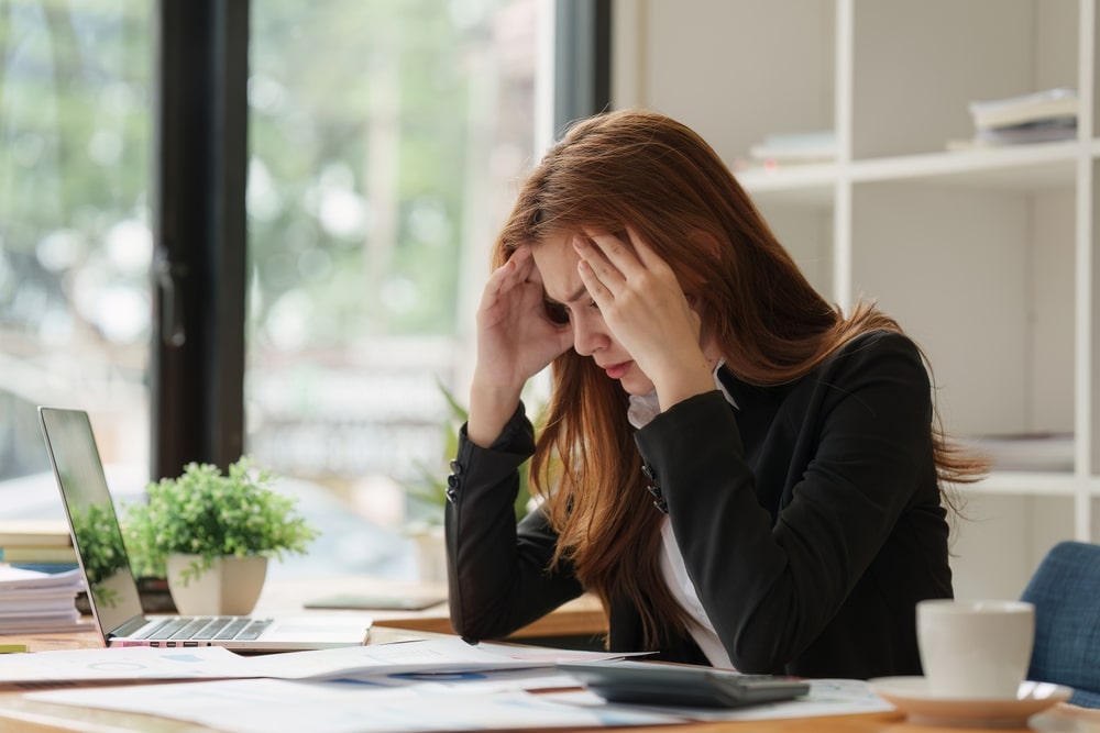 Worried woman in office holding her head while reviewing financial documents