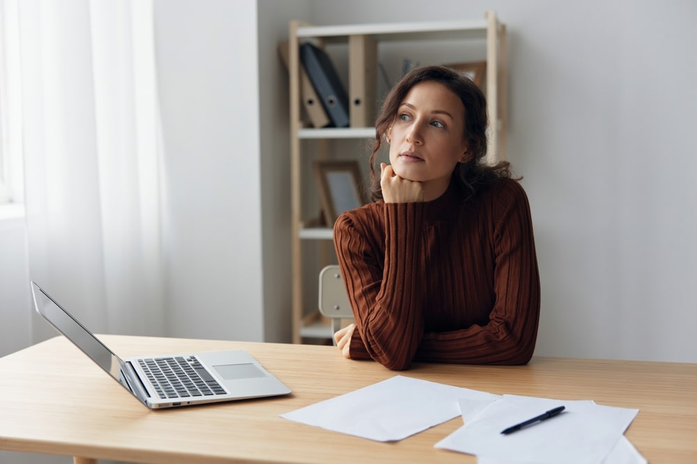 A woman is thinking about the right time to file for bankruptcy while sitting at a desk