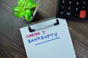 Chapter 7 bankruptcy written on a clipboard with a calculator and planted on a wooden desk