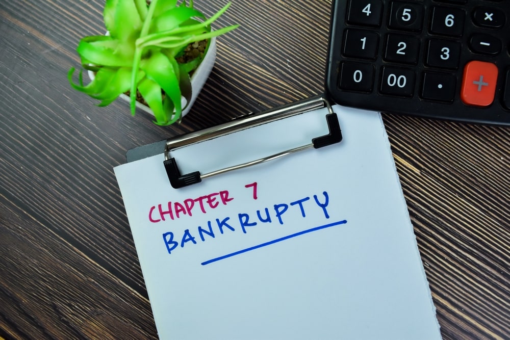 Chapter 7 bankruptcy written on a clipboard with a calculator and planted on a wooden desk