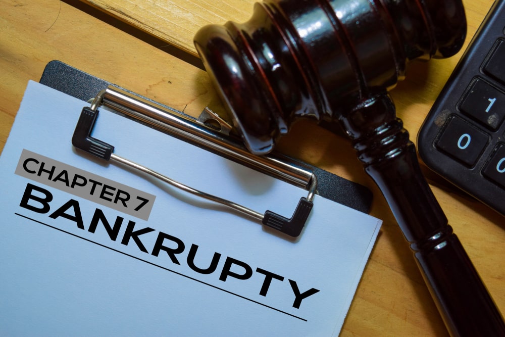Chapter 7 bankruptcy text on clipboard with judge’s gavel and calculator