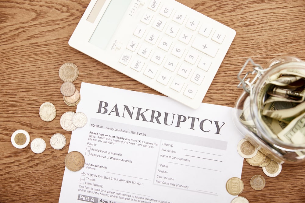 Bankruptcy form with calculator, jar of money, and coins on desk
