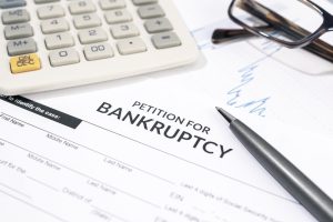 Bankruptcy petition form with pen, calculator, and eyeglasses on desk