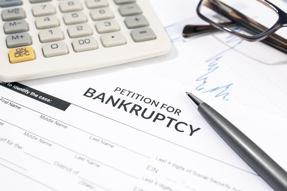 Bankruptcy petition form with pen, calculator, and eyeglasses on desk