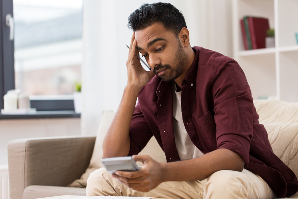 A stressed man reviewing finances with a calculator at home