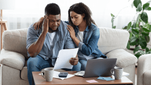 Stressed couple reviewing financial documents while researching what are the types of personal bankruptcy on laptop