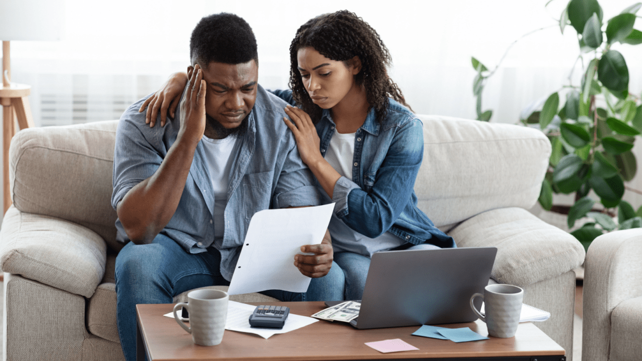 Stressed couple reviewing financial documents while researching what are the types of personal bankruptcy on laptop