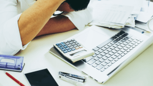 Person calculating which debts cannot be erased by bankruptcy at desk with laptop and financial documents