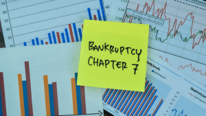 Financial charts and graphs with yellow sticky note reading "Bankruptcy Chapter 7" showing what would disqualify me from Chapter 7 eligibility considerations