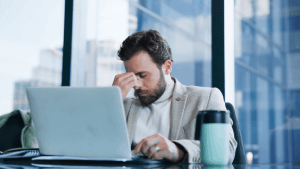 What debt never goes away concept with stressed businessman at laptop dealing with financial burden and headache in modern office