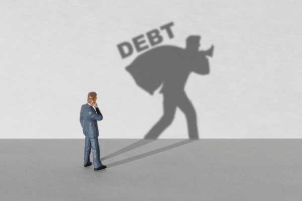 What debts cannot be forgiven concept with businessman figurine casting shadow carrying heavy DEBT burden on gray background
