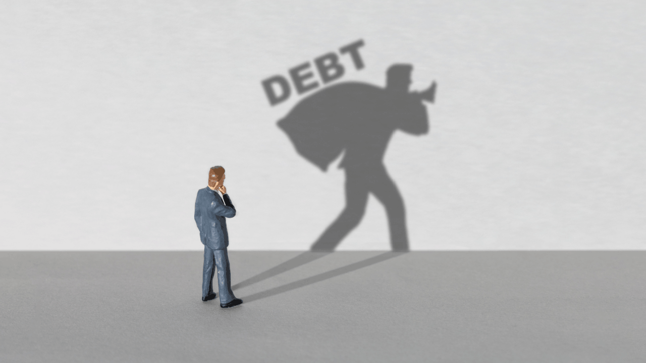 What debts cannot be forgiven concept with businessman figurine casting shadow carrying heavy DEBT burden on gray background
