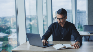 Man researching what is chapter 11 bankruptcy on a laptop with an open notebook in a modern office