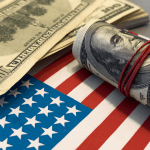 Roll of $100 bills secured with a red rubber band resting on an American flag alongside scattered currency