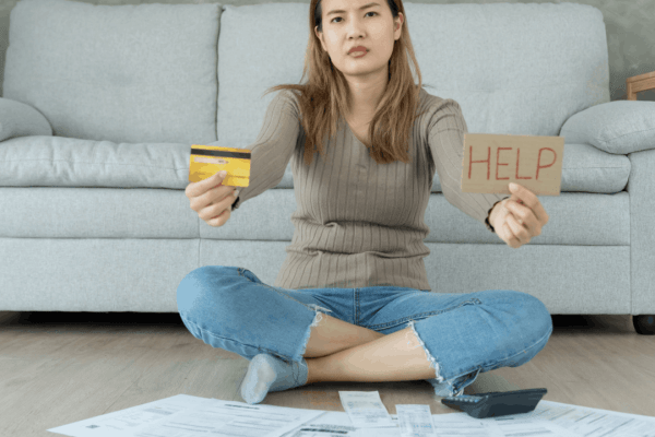 Woman holding credit card and HELP sign surrounded by bills